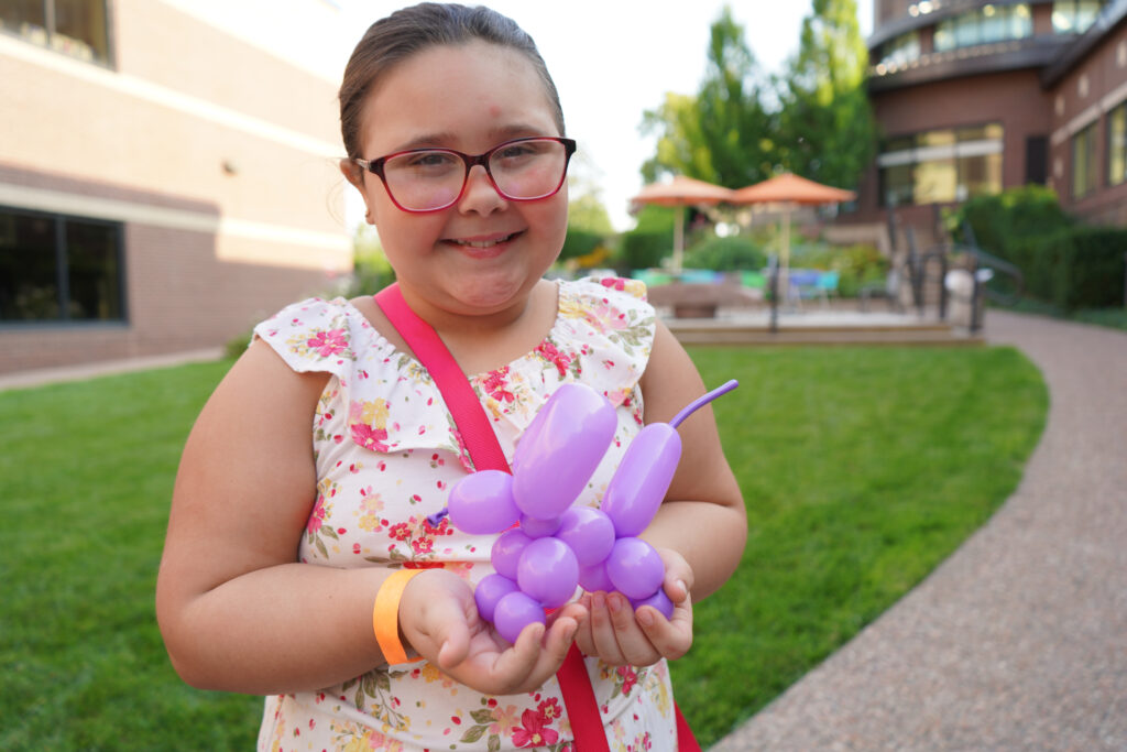 Girl poses for a photo while holding a balloon animal. 