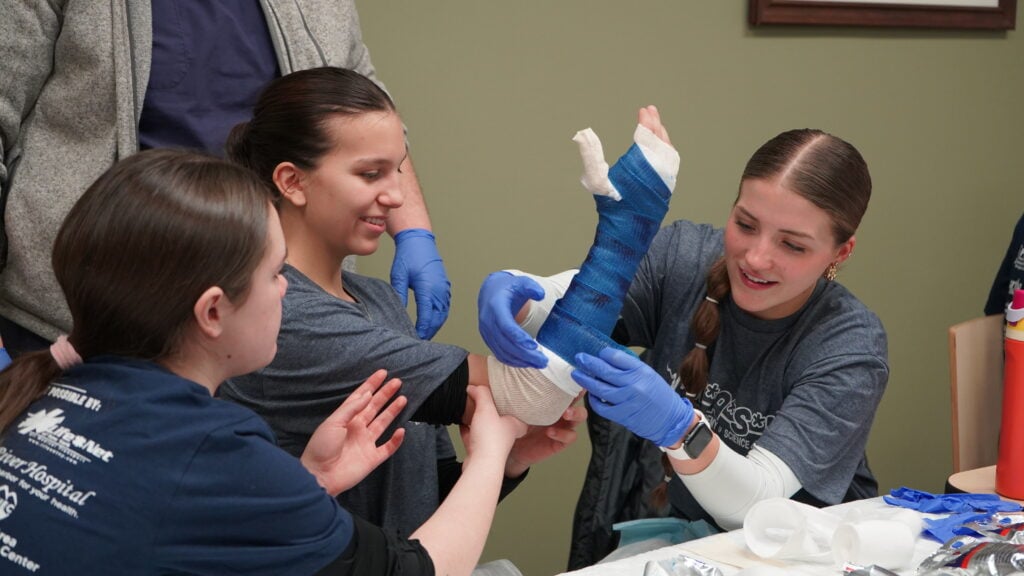 Photo of three MASH Camp students learning how to make a cast on an arm