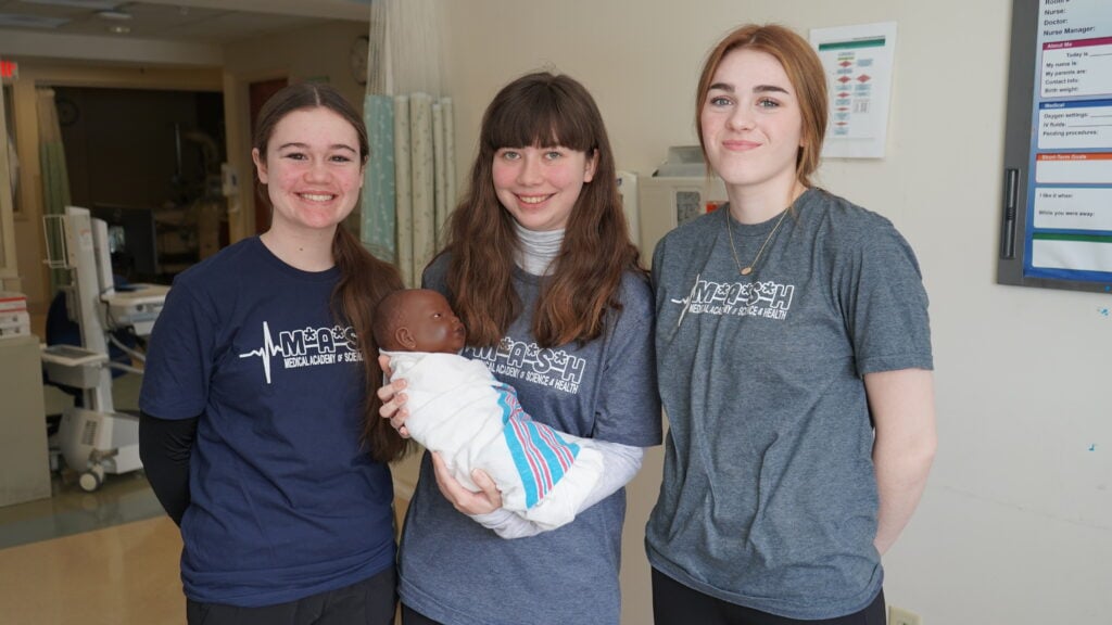 Three MASH Camp Students pose for a photo with an educational practice baby