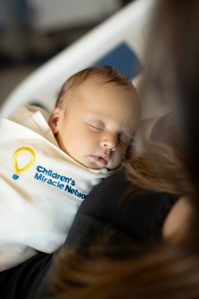 A swaddled baby sleeps with the Children's Miracle Network logo on his swaddle