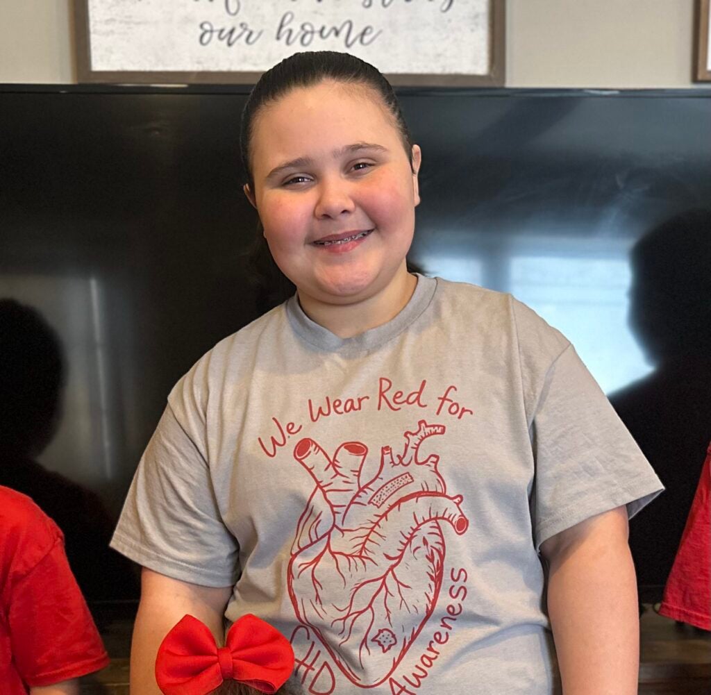 Olivia Gorman, a CMN kid, smiles while wearing a heart health t-shirt