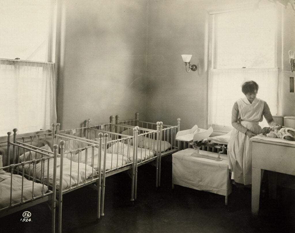 Archival photo of Samaritan's nursey with a nurse and several babies in cribs